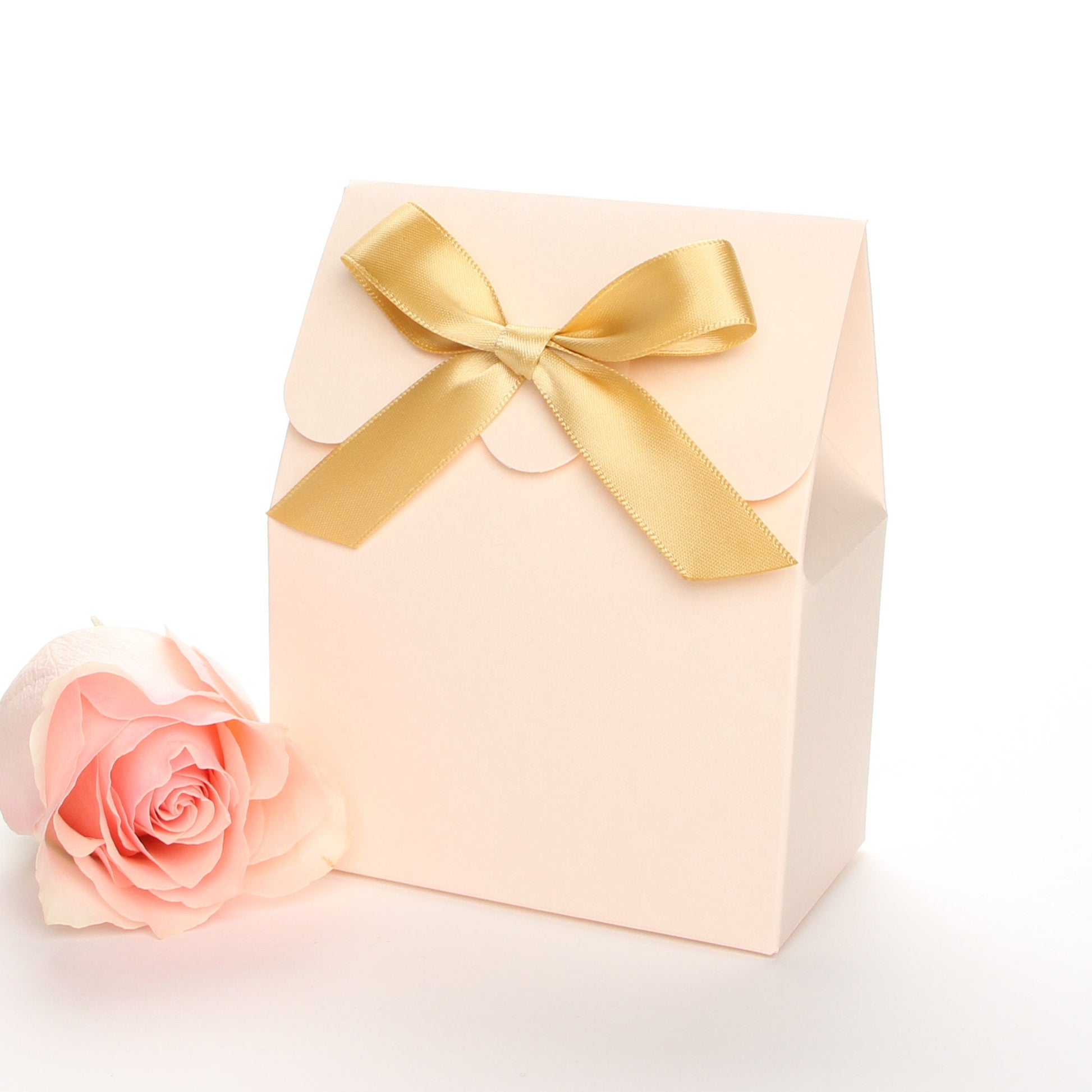 Lux Party’s blush favor box with a scalloped edge and a gold bow next to a pink rose.