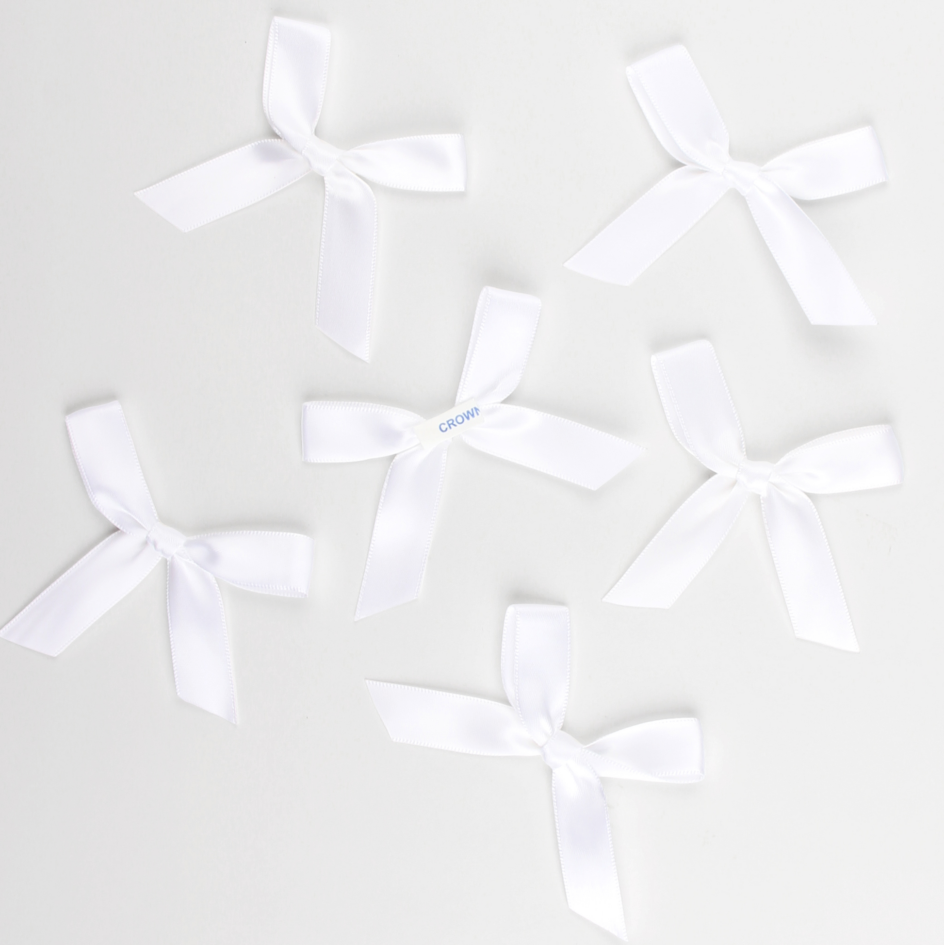 Multiple white satin pre-tied bows by Lux Party, showing peel and stick backing.