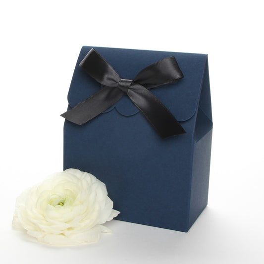 Lux Party’s navy blue favor box with a scalloped edge and a black satin bow next to white ranunculus flowers.