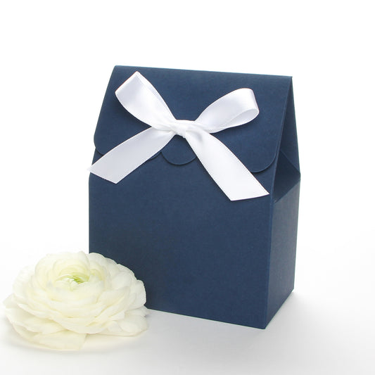 Lux Party’s navy blue favor box with a scalloped edge and a white satin bow next to white ranunculus flowers.