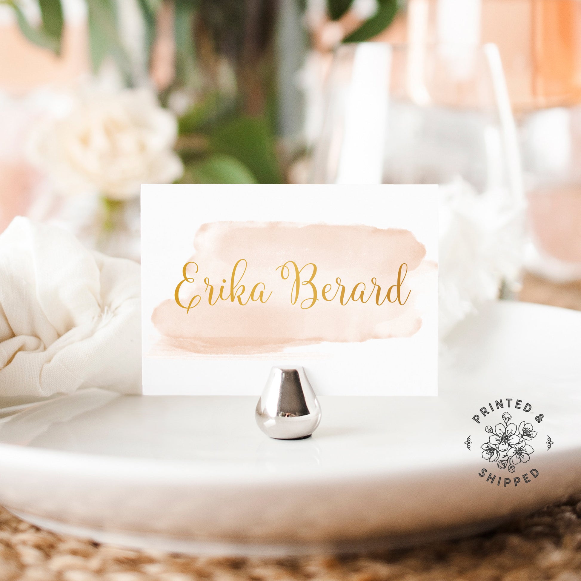 Lux Party’s gold and blush place cards with blush watercolor background and gold lettering, in a wedding table place setting.