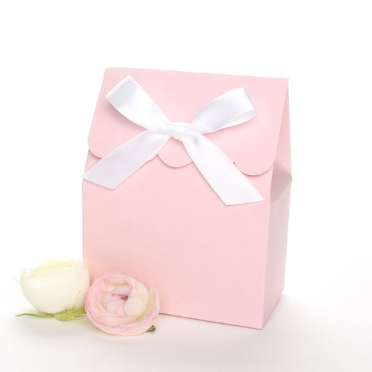 Lux Party’s pink favor box with a scalloped edge and a white bow next to pink and white ranunculus flowers.