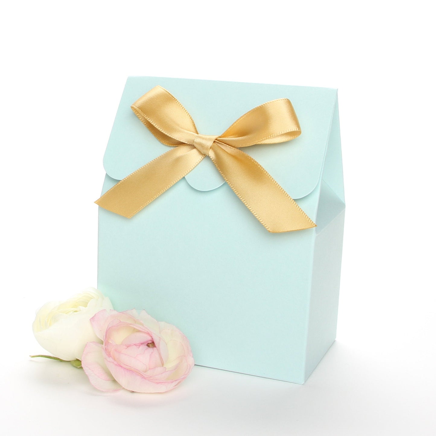 Lux Party’s light blue favor box with a scalloped edge and a gold satin bow next to pink and white ranunculus flowers.