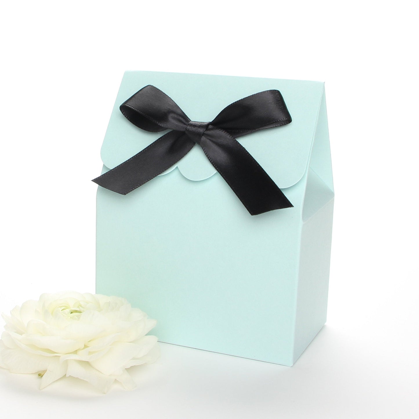 Lux Party’s light blue favor box with a scalloped edge and a black satin bow next to white ranunculus flowers.