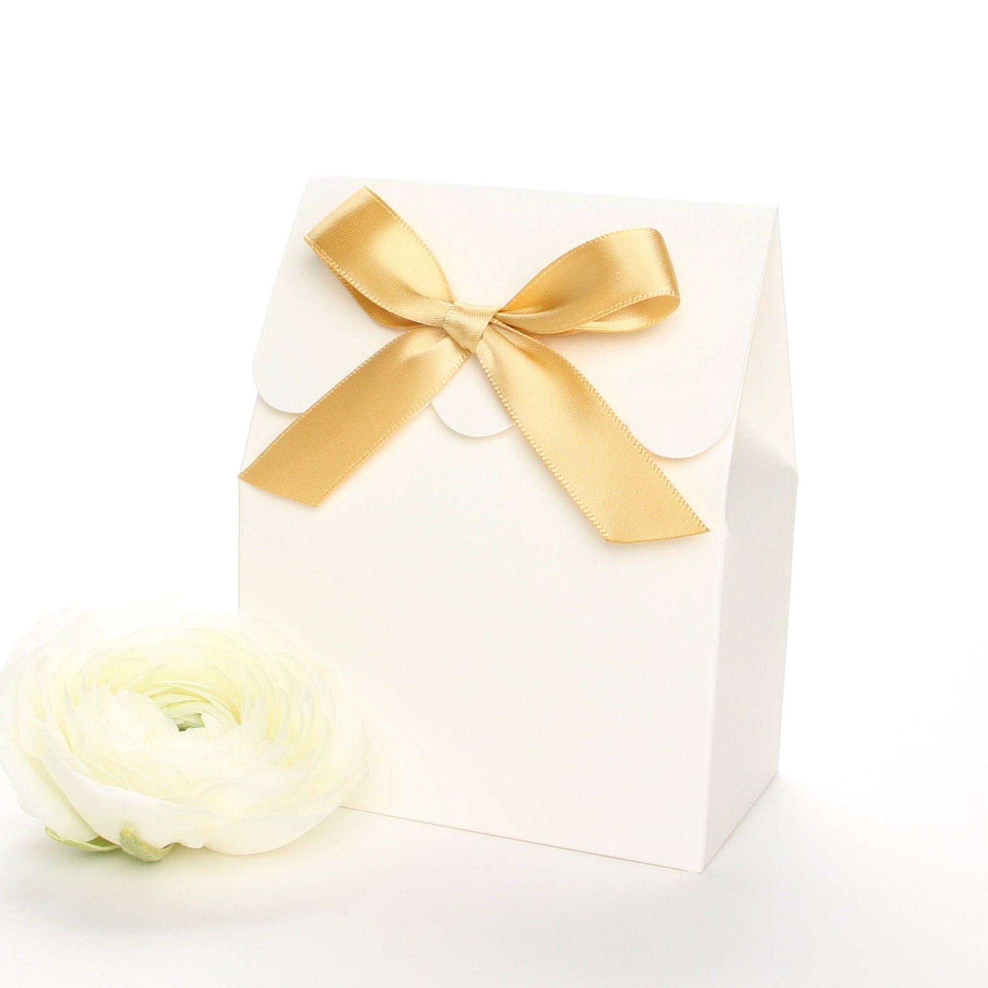 Lux Party’s ivory favor box with a scalloped edge and a gold satin bow next to white ranunculus flowers.